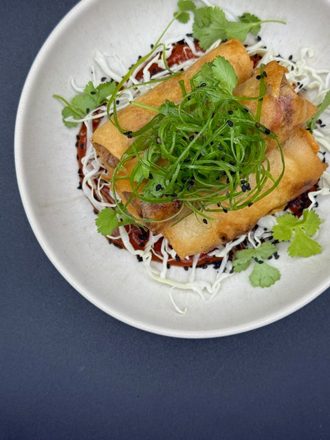3 Frühlingsrollen appetitlich auf einem weißen Teller angerichtet. Mit einem roten Curryketchup der Marke Syltico und etwas weißem Spitzkohl. Getopt wurden die Frühlingrollem mit Sesam, Frühlingslauch und Koriander.